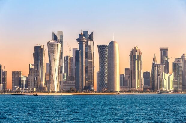 Modern skyline of Qatar with tall buildings and blue sea under clear sky