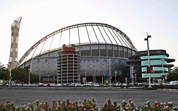 Modern stadium architecture in Qatar with surrounding buildings and parked cars