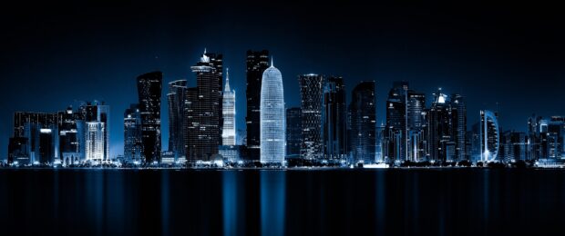 Night view of Qatar city skyline with illuminated skyscrapers reflecting on the water