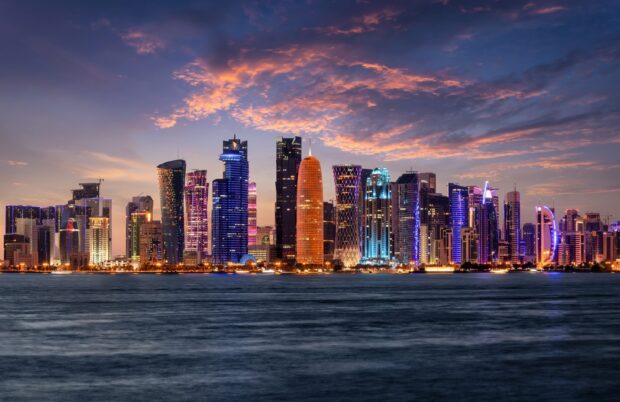Qatar cityscape at sunset with colorful illuminated skyscrapers and calm water in the foreground