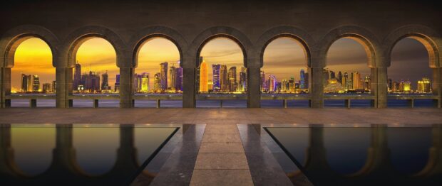 View of Qatar cityscape through stone arches during sunset with vibrant lights