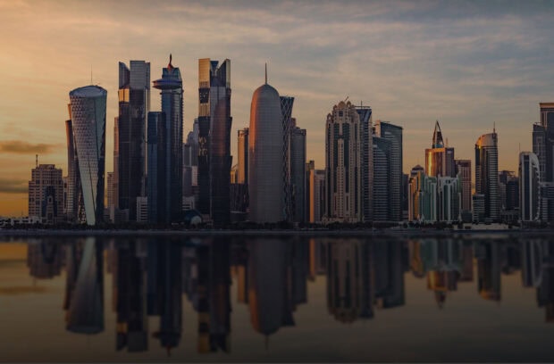 Modern Qatar cityscape with high rise buildings reflecting on calm water at sunset