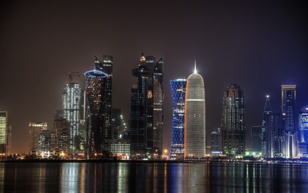 Modern Qatar skyline at night with illuminated high rise buildings and reflections on water