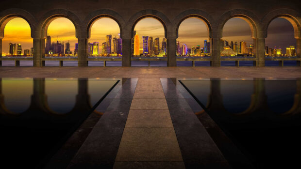 View of Qatar city skyline from arches at sunset with reflections in water