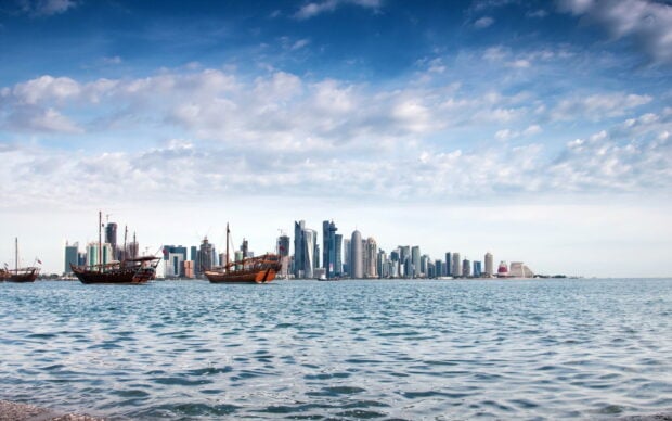 Traditional boats in Qatar skyline with modern buildings under cloudy sky