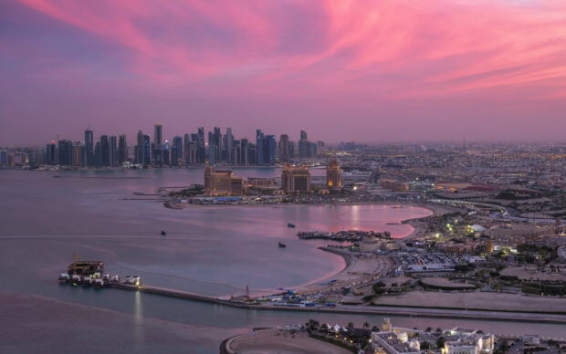 A panoramic view of Qatar cityscape during sunset with pink sky and calm waters