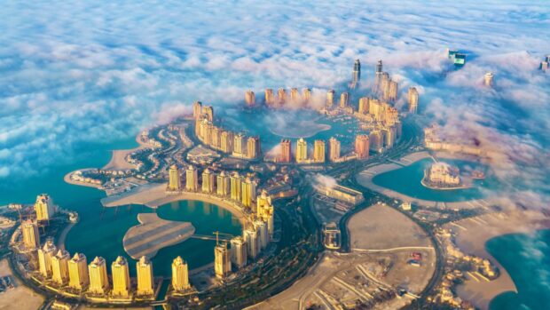Aerial view of Qatar cityscape with modern buildings surrounded by water and morning mist