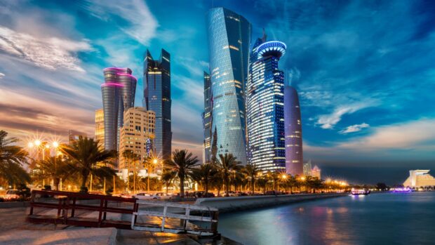 Modern architecture skyline in Qatar during sunset with illuminated skyscrapers and palm trees