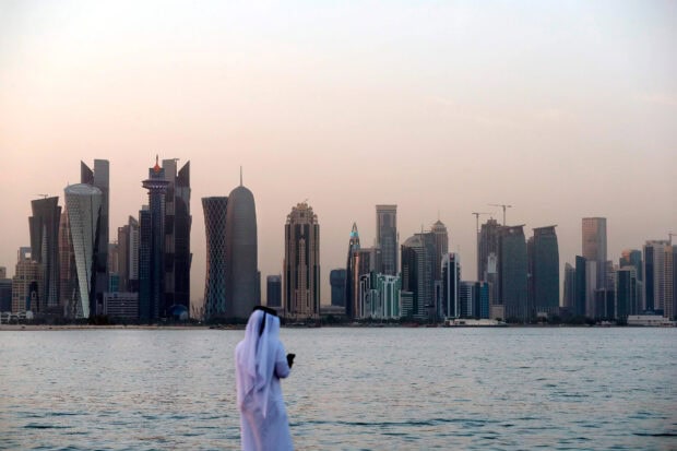 A man in traditional clothing overlooking Qatar city skyline at dusk