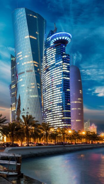 Modern Qatar cityscape with illuminated skyscrapers and palm trees at dusk