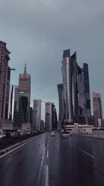 Modern Qatar cityscape with skyscrapers and wet road under cloudy sky