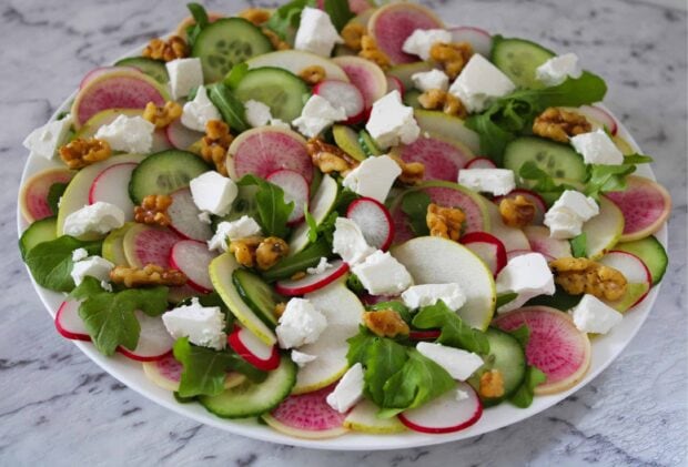 Fresh radish slices with cucumber lettuce walnuts and cheese on a white plate