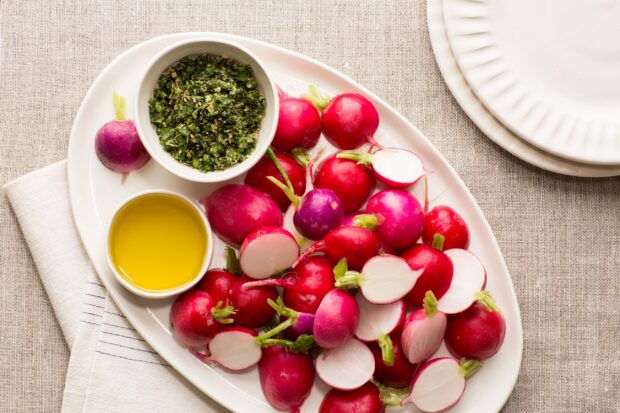 Fresh radish arranged on a plate with herb seasoning and olive oil on the side