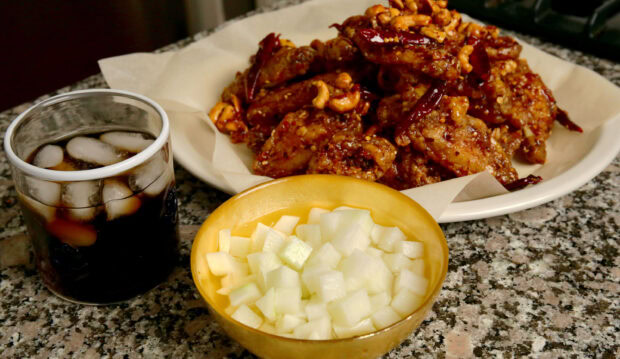 A bowl of diced radish served on a granite table alongside spicy chicken wings and a glass of iced cola