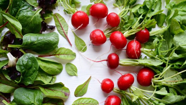 Fresh radish arranged with green leaves on a white wooden surface