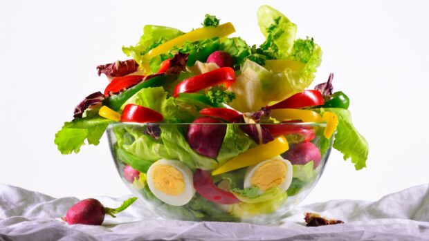 A fresh radish mixed salad with lettuce bell peppers and boiled eggs in a glass bowl