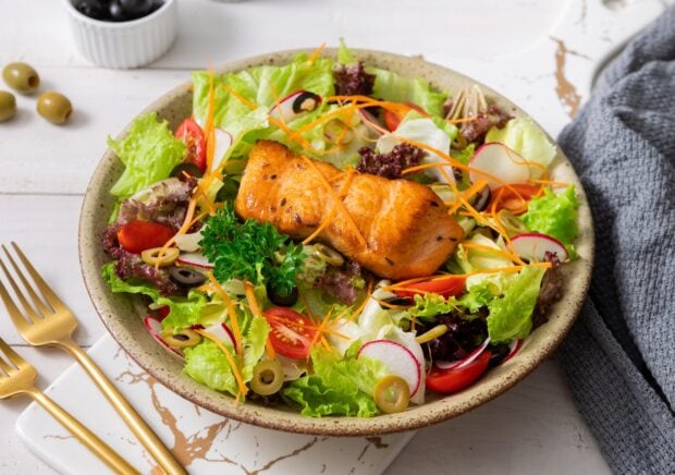 Fresh radish slices in a healthy salad bowl with grilled salmon and mixed greens