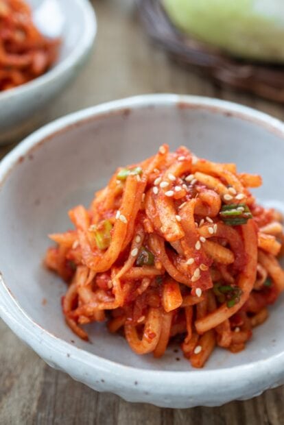 Spicy radish dish with sesame seeds in a bowl on wooden table