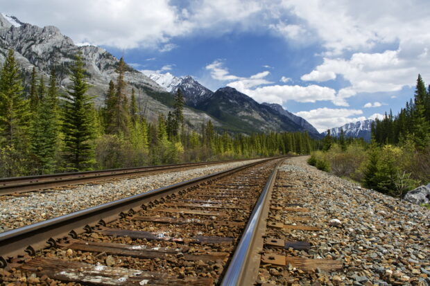 Railway tracks running through forested mountains with clear blue sky and clouds