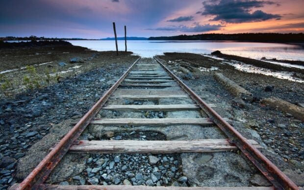 Abandoned railway tracks leading into the sea during a colorful sunset