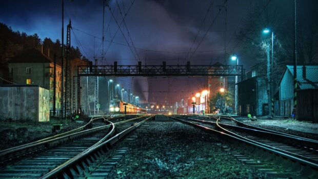 Nighttime railway tracks with a train approaching near urban buildings and street lights
