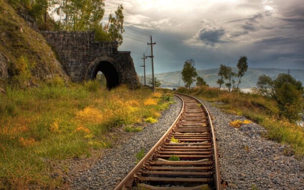 Old railway track leading to a stone tunnel surrounded by grass and trees