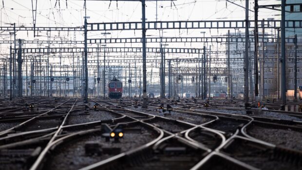 Complex railway tracks and overhead wires with a red locomotive in the distance