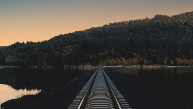 Railway track surrounded by forest and lake at sunset with scenic mountain landscape