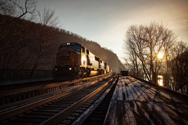 A diesel locomotive on railway tracks passing through a mountainous area at sunset