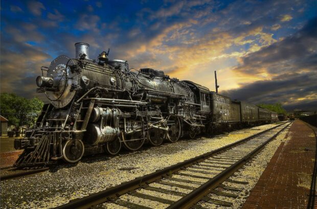 Vintage steam locomotive on railway tracks under a dramatic sky at sunset