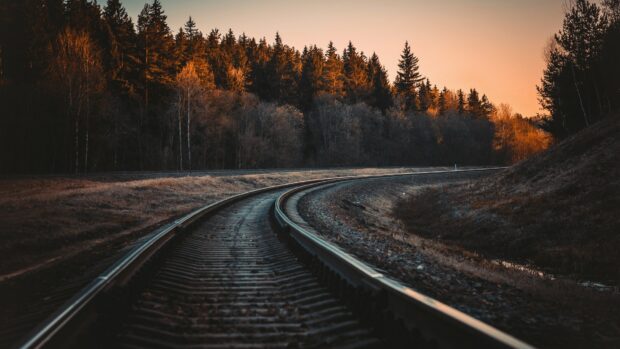 A winding railway track passing through a forest during sunset with orange light on trees