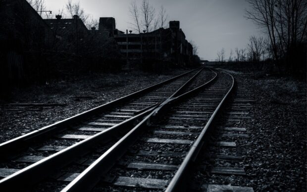 Abandoned railway tracks extending through a gloomy industrial area with leafless trees