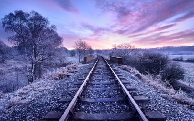 Frost covered railway track surrounded by bare trees in a winter landscape at sunrise