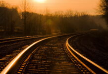 Golden sunlight reflecting on railway tracks in a peaceful forest setting at sunset