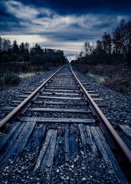 Old wooden railway track surrounded by forest and cloudy sky in the distance