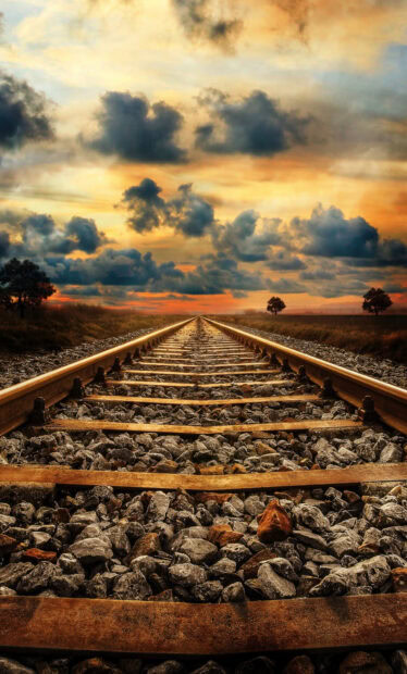 Railway tracks extending into the horizon under a dramatic cloudy sunset sky