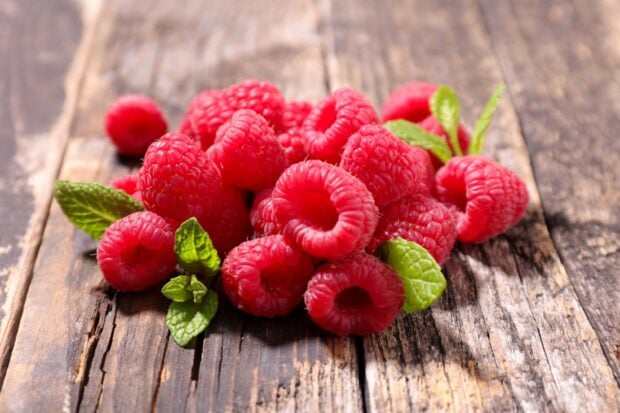 Fresh raspberry fruit with green leaves on wooden surface