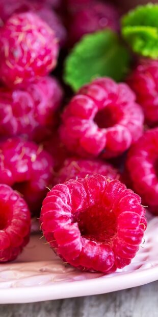 Fresh raspberry close up with green leaves on a plate for a vibrant mobile wallpaper