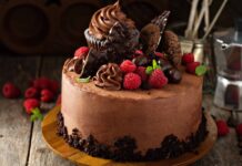 A chocolate cake topped with fresh raspberry and chocolate decorations on a wooden surface