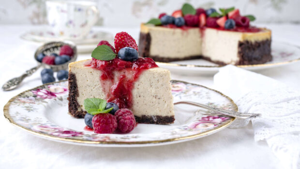 A slice of cheesecake topped with raspberry sauce and fresh raspberries on a decorative plate