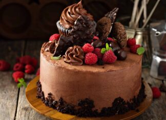 A chocolate cake topped with fresh raspberry and chocolate decorations on a wooden surface