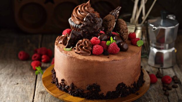 A chocolate cake topped with fresh raspberry and chocolate decorations on a wooden surface