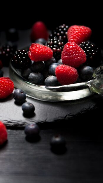 Fresh ripe raspberry with blueberries and blackberries in a glass bowl on a dark surface