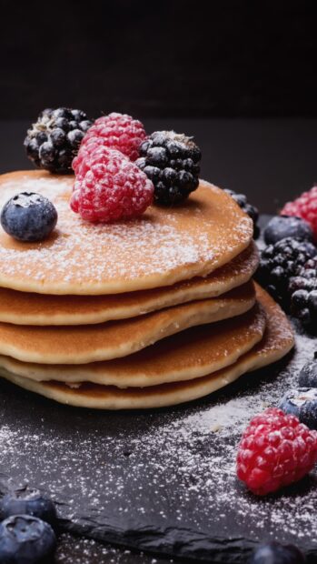Fresh raspberry and berries dusted with powdered sugar on pancakes