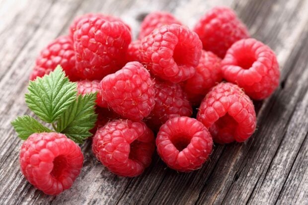 Fresh raspberry fruit with green leaves on wooden surface