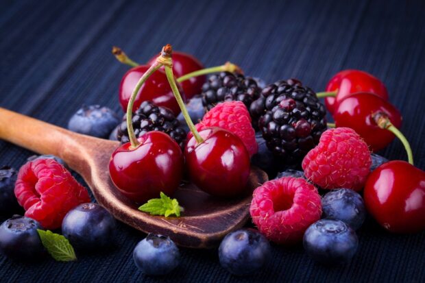 Fresh raspberry fruits placed among cherries and blueberries on a wooden spoon