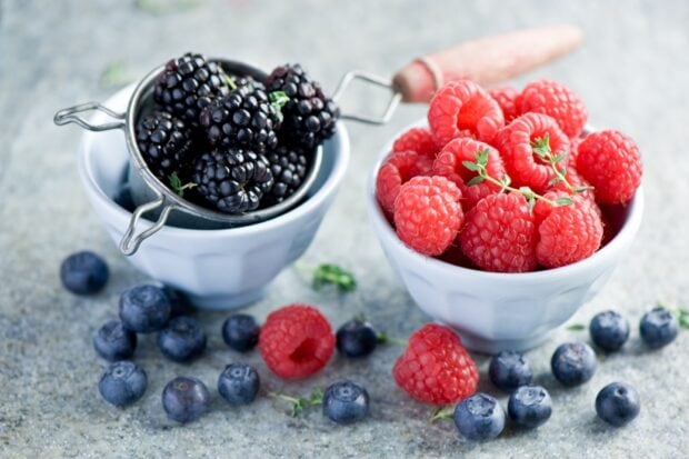 Fresh raspberry with blueberries and blackberries in white bowls on a textured surface