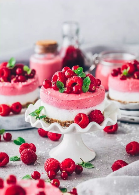 A delicious raspberry dessert topped with fresh berries and mint leaves on a white cake stand