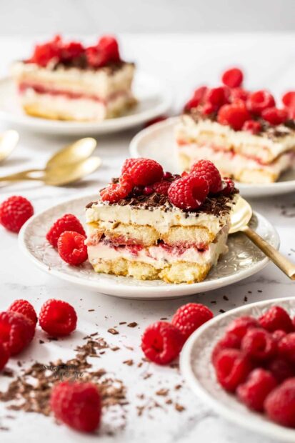 A delicious dessert with fresh raspberry layers and cream on a white plate with scattered raspberries