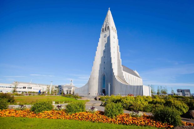 The unique Reykjavik architecture stands tall against a clear blue sky with colorful flowers in the foreground